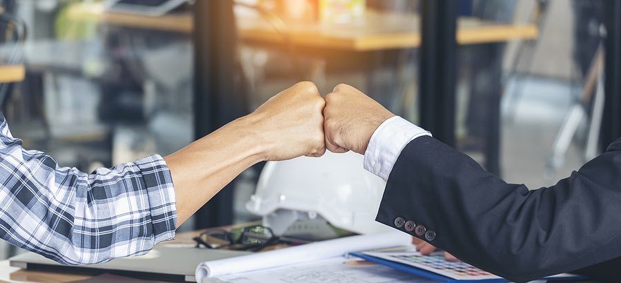 Arms of two men in a business meeting giving a fist bump on the table, showing teamwork and support.
