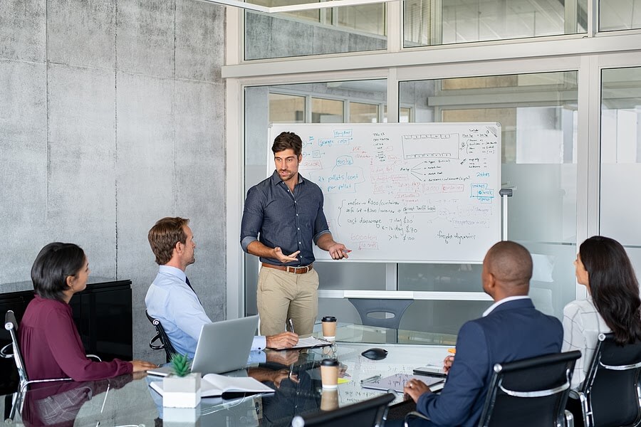 Group-of-team-members-getting-trained-in-a-conference-room-by-a-man-with-glasses