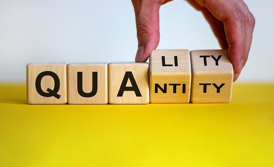 Wood blocks on a yellow table that spell out “quantity” and “quality when the last two blocks are being turned over