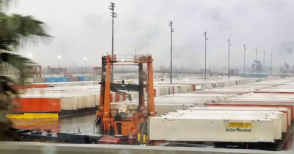 Over 100 semi trucks with shipping containers parked in a parking lot waiting to be transported